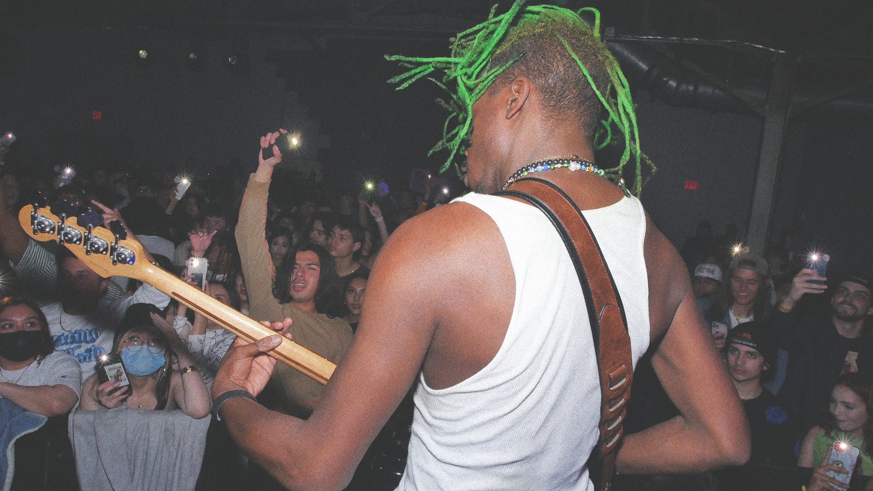 A bassist seen from behind leaning out over a crowd holding up phones