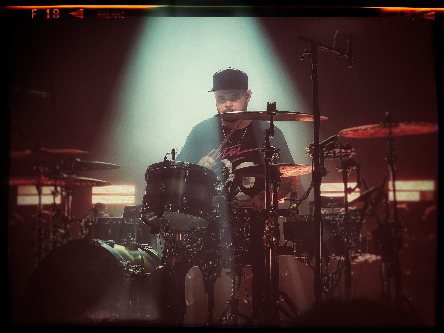 A drummer behind a large kit, lit from behind by a single beam through haze