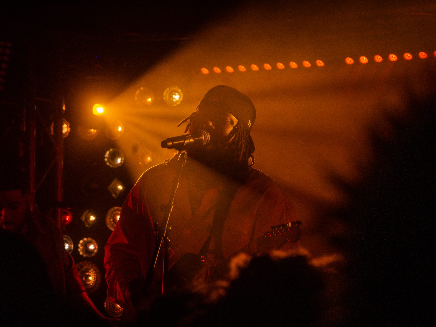 A wide shot of a singer silhouetted under a row of warm stage lights