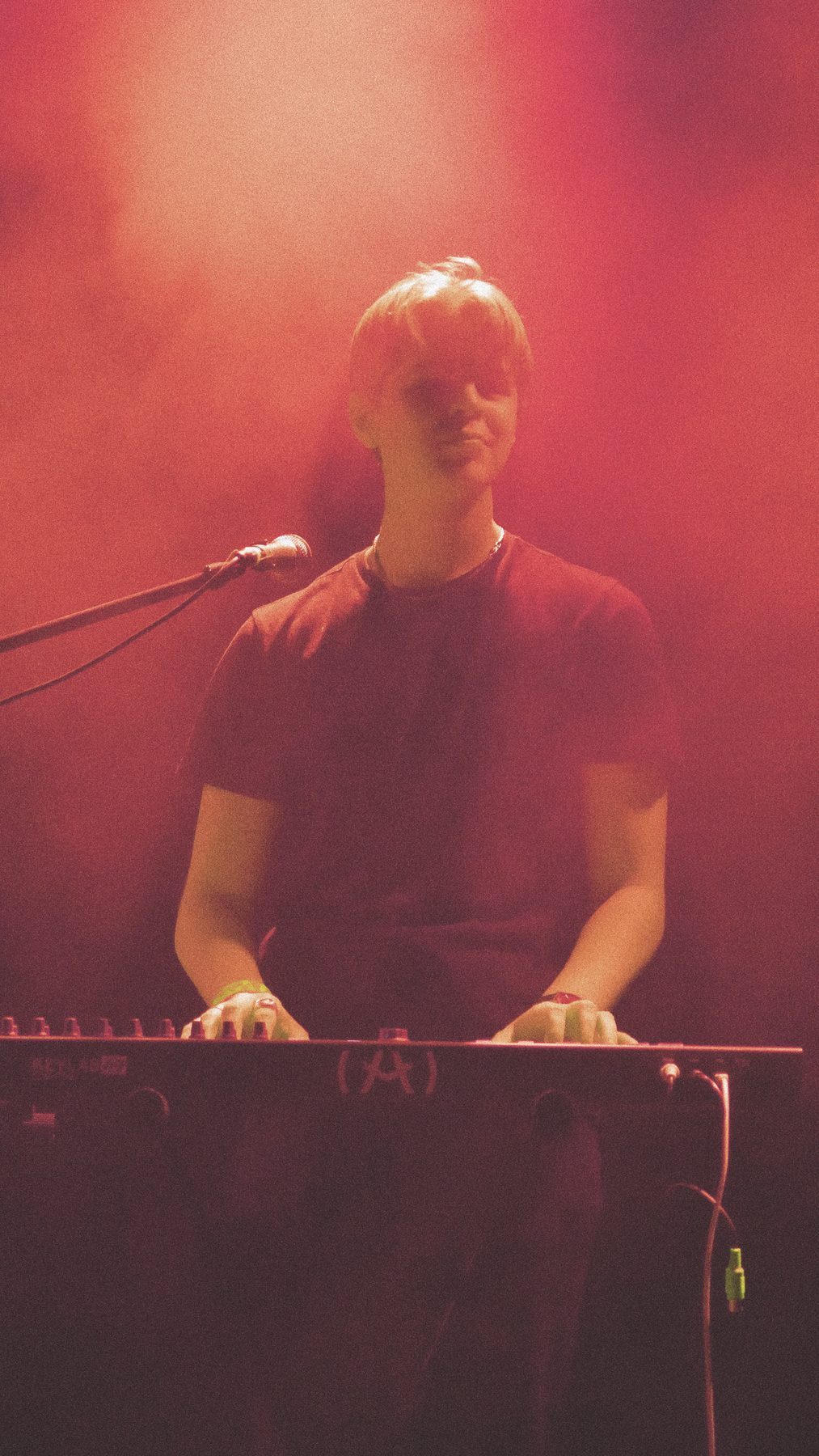 A keyboard player under deep red stage light, hands on the keys