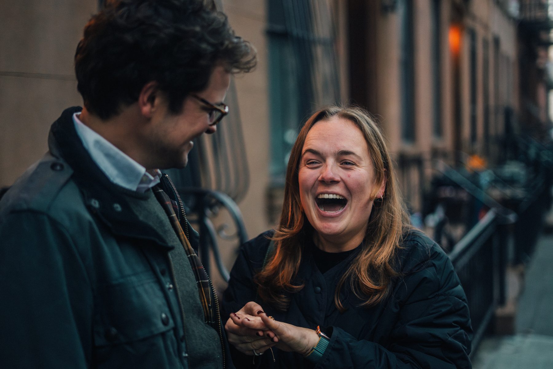 A woman laughing wide with a ring in her palm, a man beside her smiling down