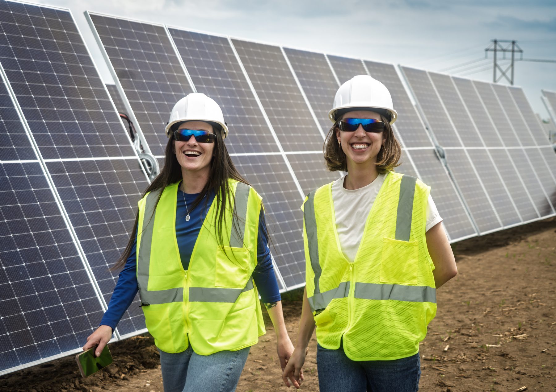 Two crew members in hard hats and safety vests walking beside a row of solar panels