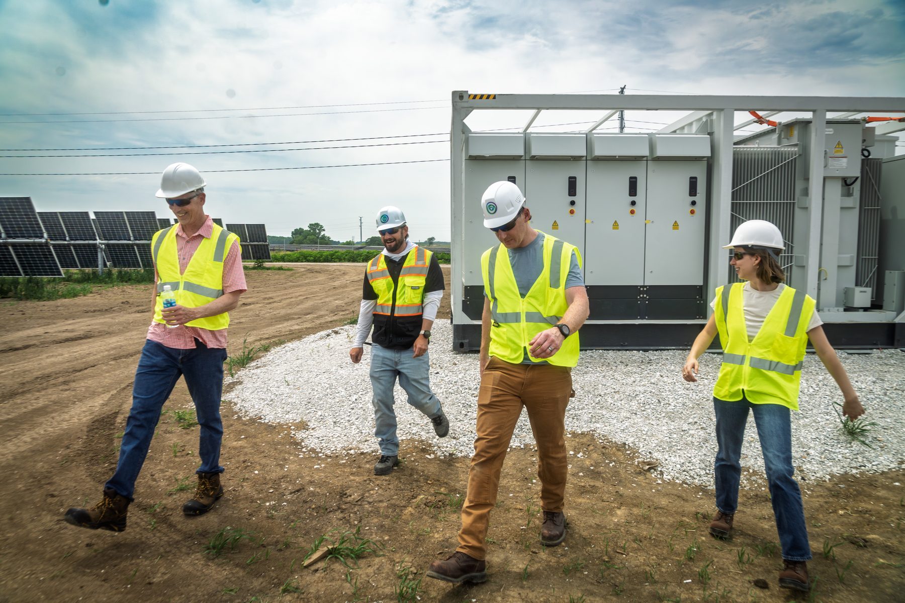 Four people in hard hats and safety vests walking a solar site