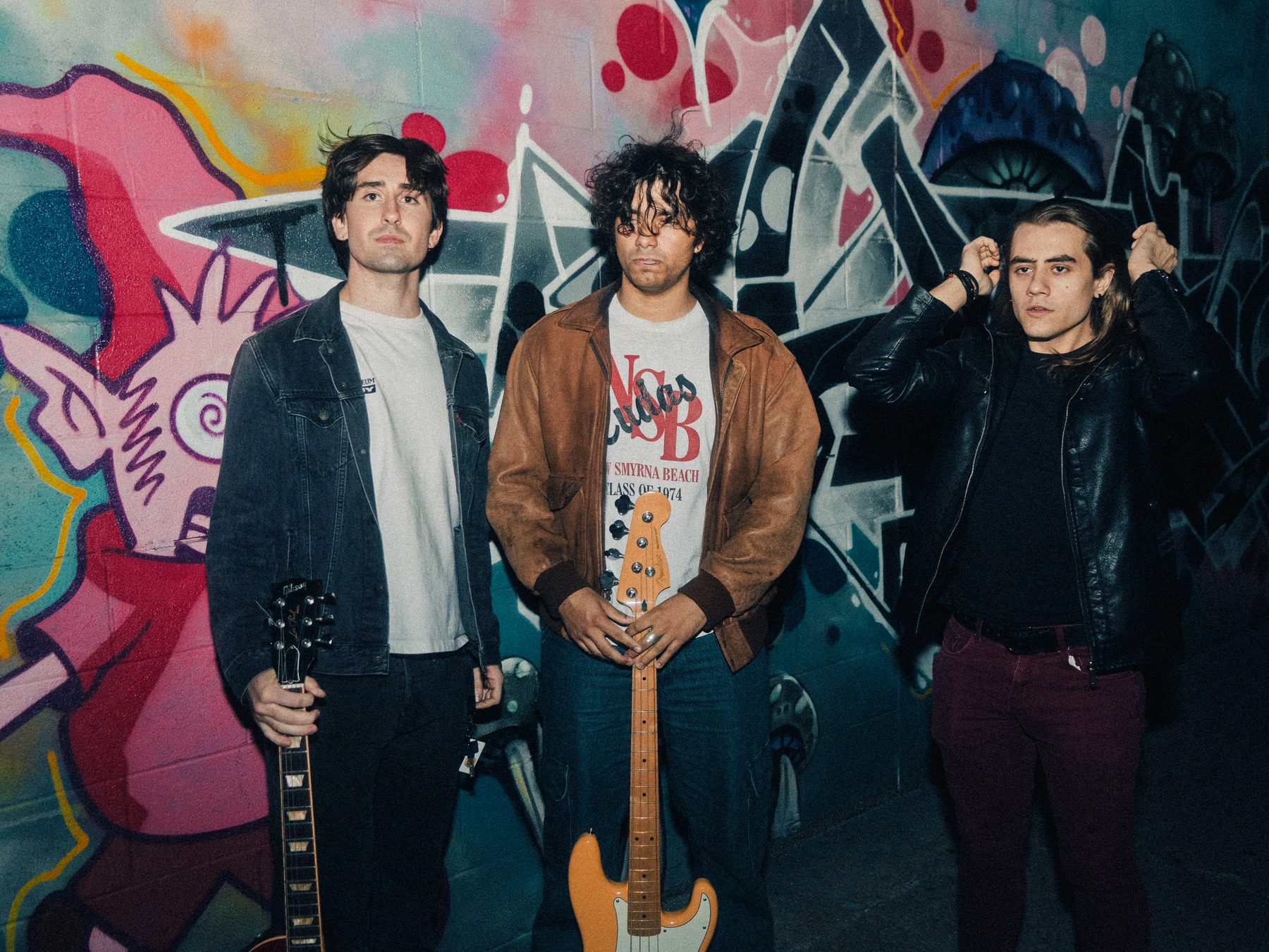 Three band members with guitars standing in front of a graffiti mural